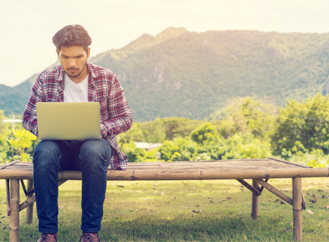 Man on laptop sitting on a bench in a scenic environment